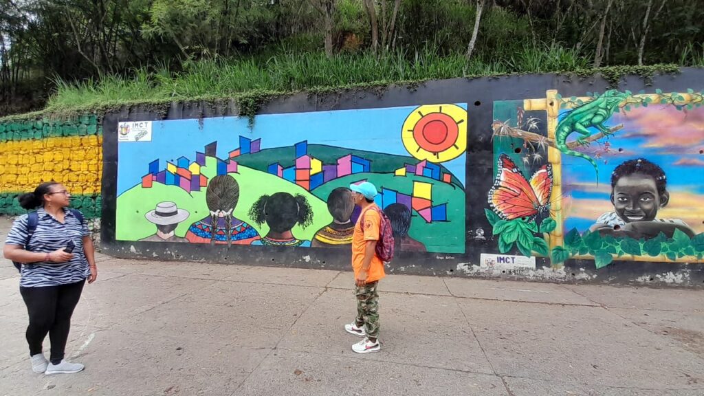 Personas observan mural urbano con paisajes coloridos y retrato realista